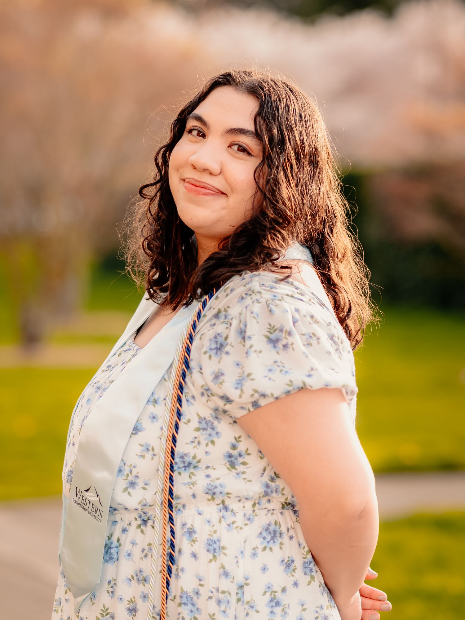 Portrait of someone in a floral dress smiling against a blurred spring background.