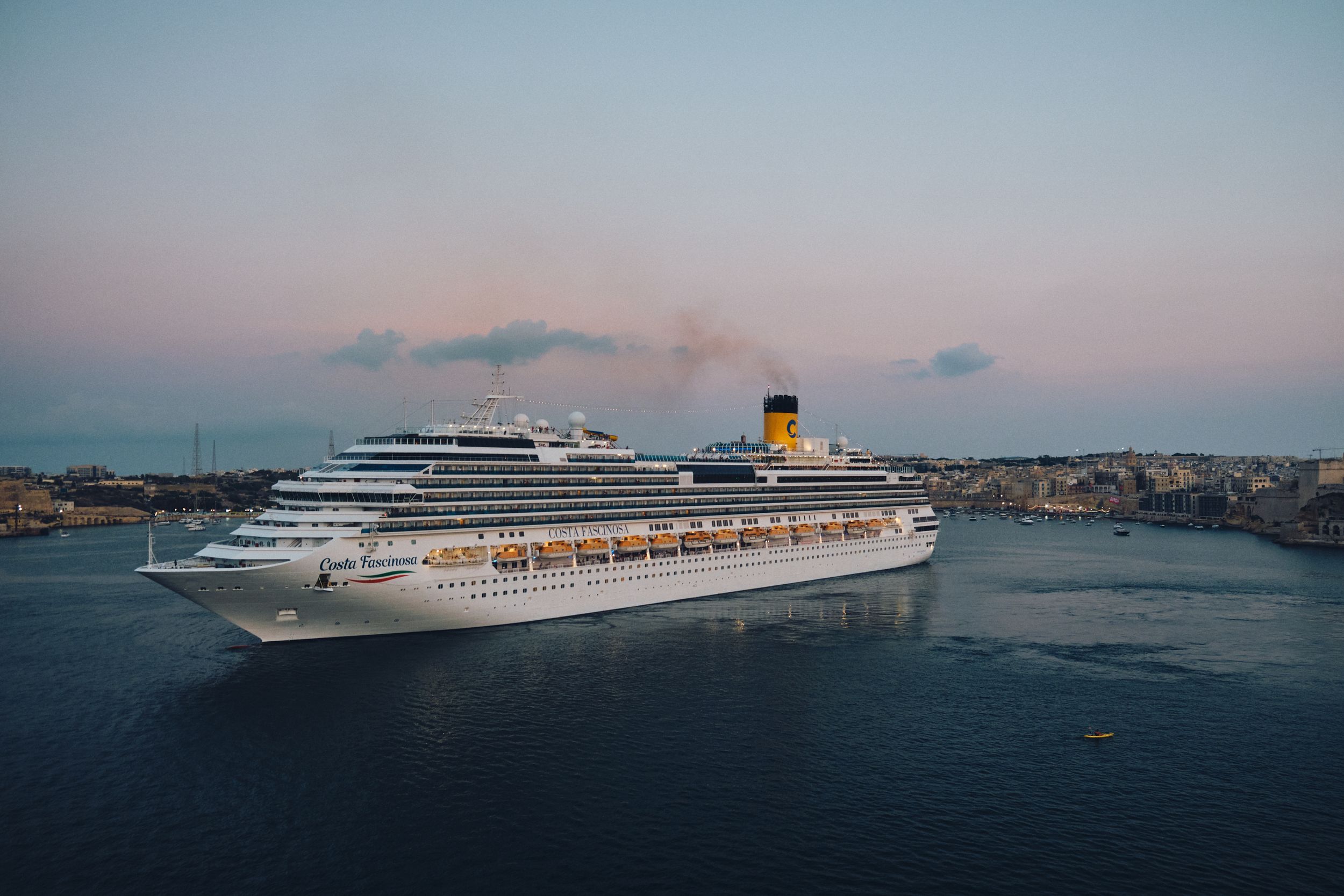 A large Costa cruise ship anchored in Malta's Grand Harbor during sunset.