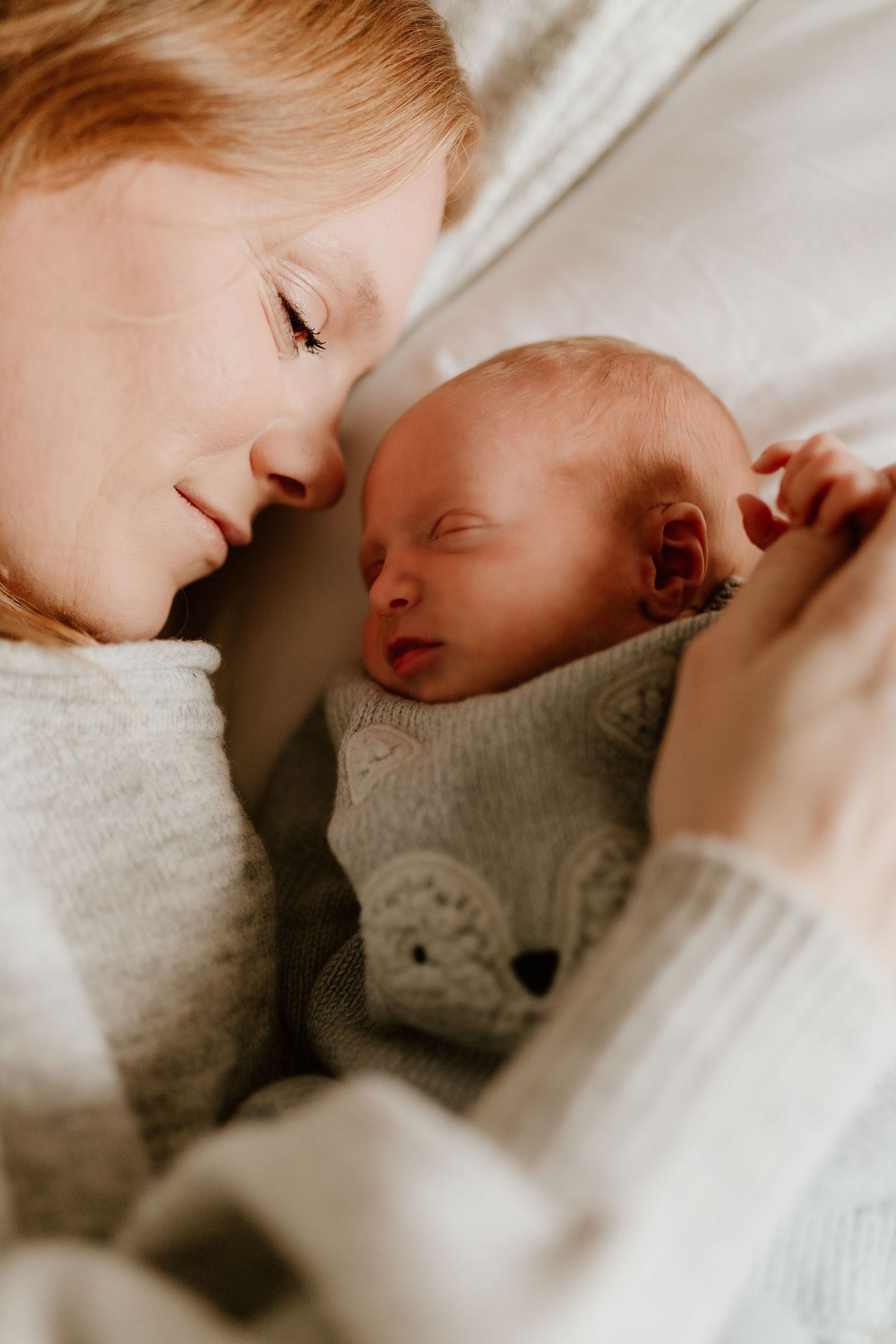 a close up photo of a new mom lying on the bed with her newborn baby, holding the baby's hand
