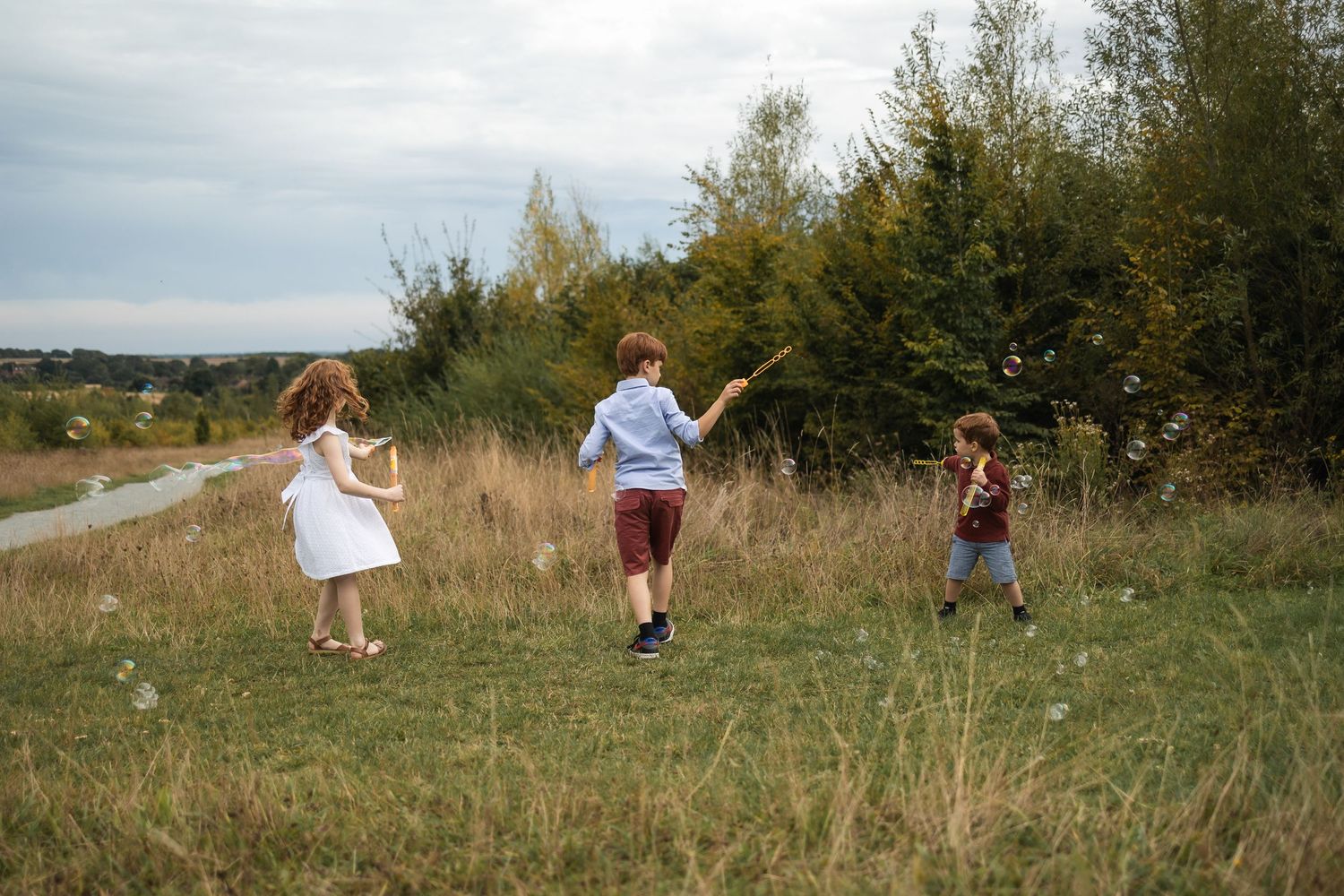 Three young children on a photoshoot in Regents Park in London with Jane Nicholson Photography, playing with bubbles.