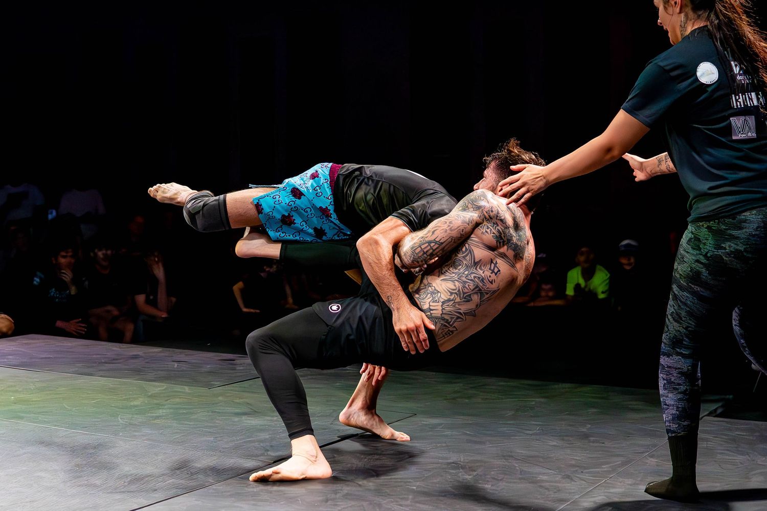 Two performers demonstrate an acrobatic dance move on a dark stage during a performance.