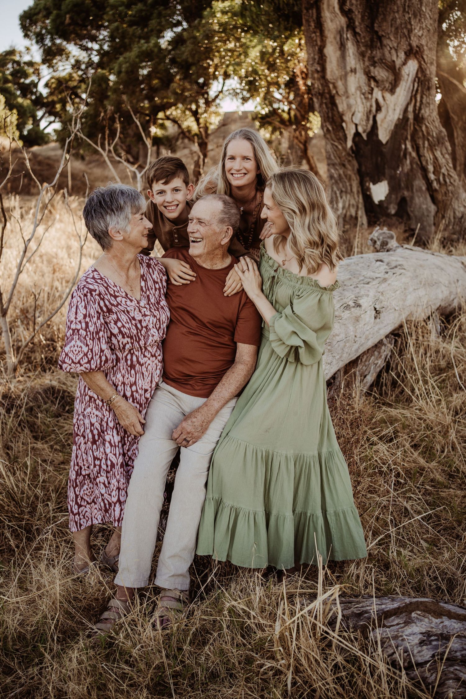 Family group wearing coordinated earth-tone outfits posing together in natural outdoor setting.