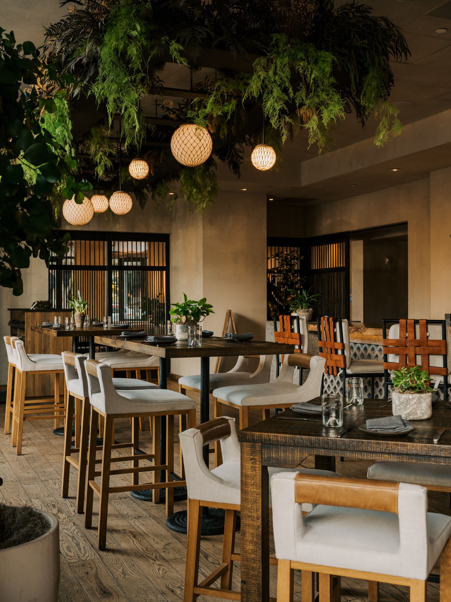Upscale bar area featuring woven pendant lights, hanging plants, and comfortable upholstered bar seating.