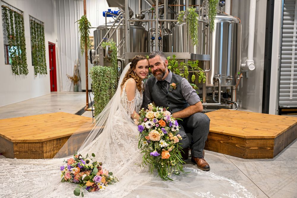 Bride and groom smiling together inside rustic brewery wedding venue with industrial brewing tanks.