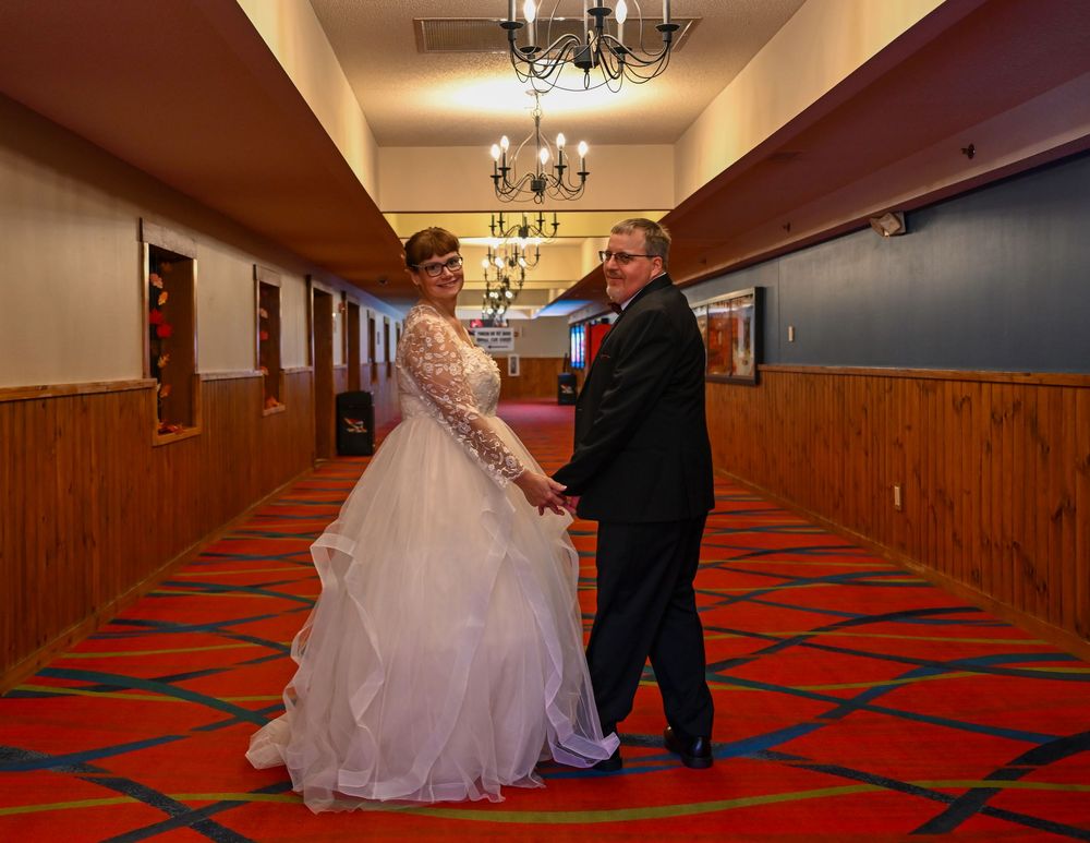 Wedding couple holding hands and posing in a hallway with red carpet and wood paneling.