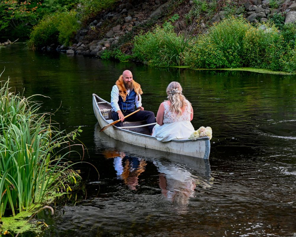 Bride and groom in a canoe on a serene river surrounded by lush greenery on their wedding day.
