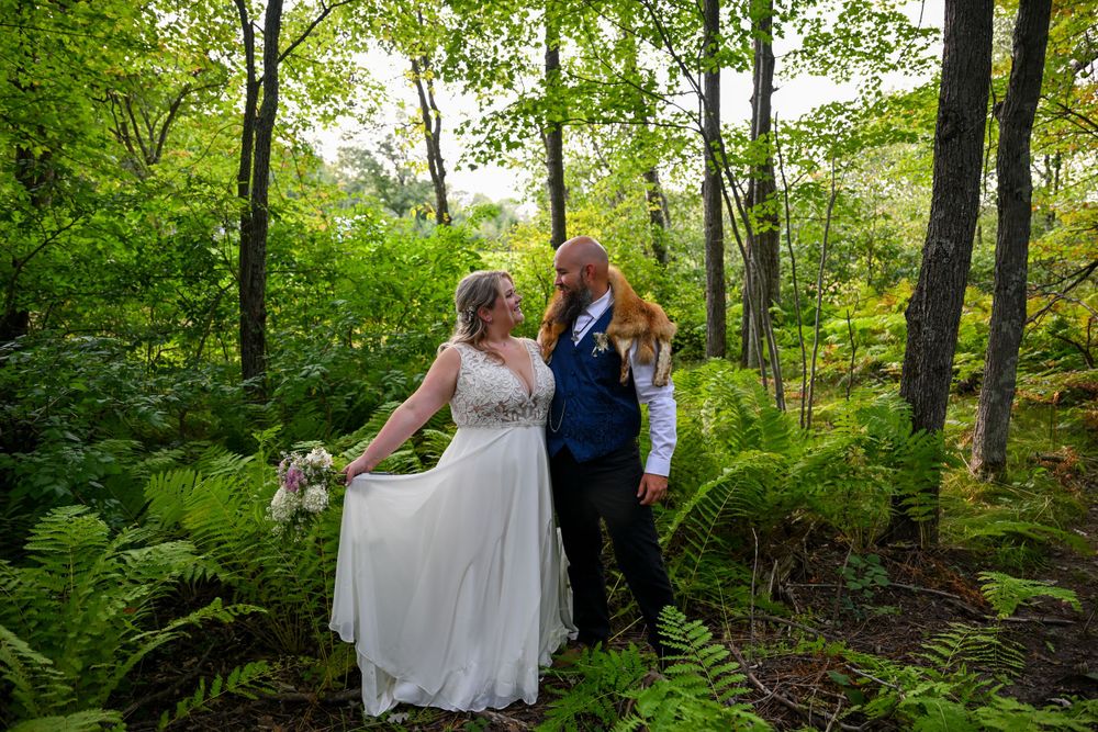 Bride holding bouquet and groom sharing a tender moment surrounded by lush green ferns in a forest.