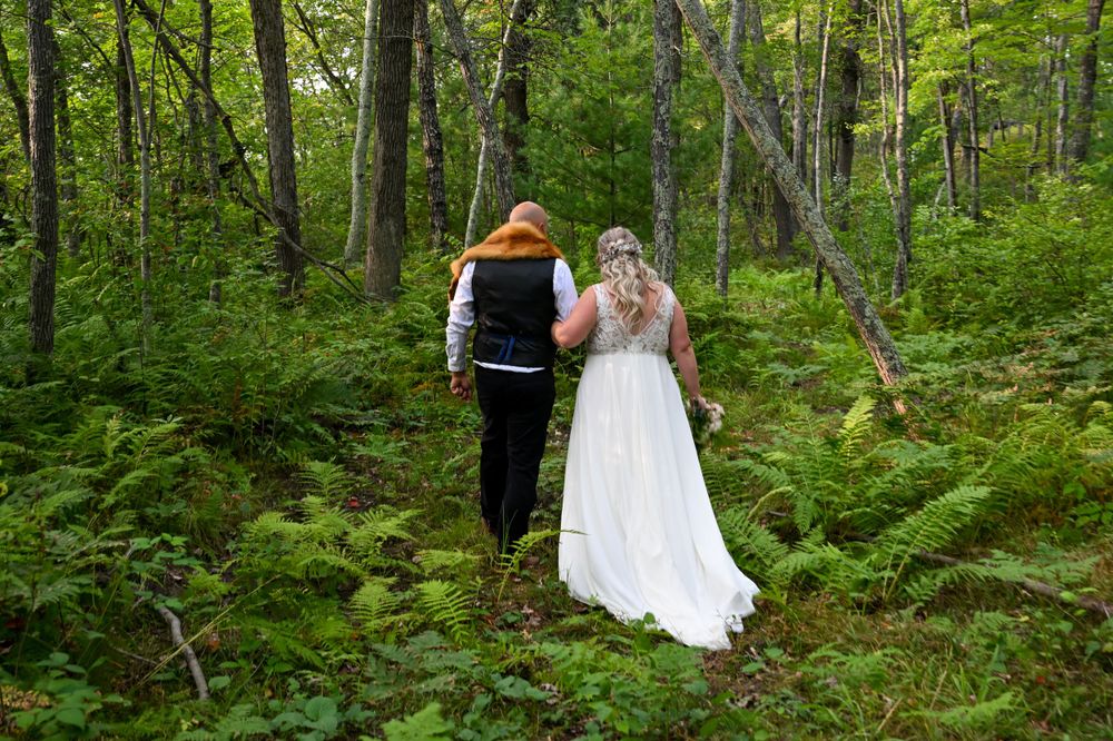 Bride in white gown and groom walking hand in hand through a lush green forest on their wedding day.