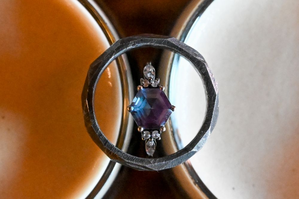 Hexagonal blue sapphire engagement ring with diamond accents inside silver wedding band on brown surface.