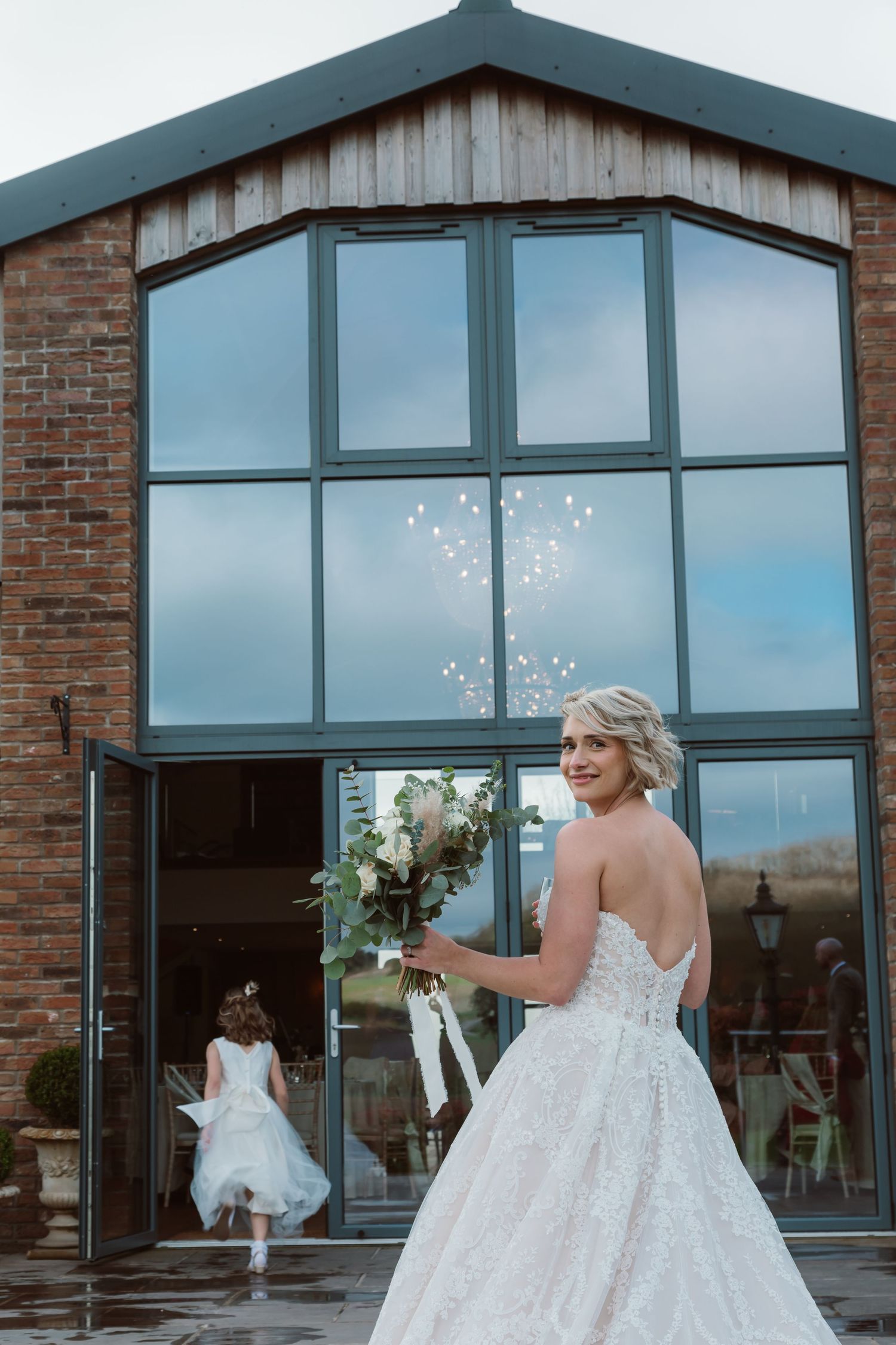 A bride in a flowing white ballgown twirls joyfully in front of large windows at a rustic brick venue. Photographer. Hull. East Yorkshire.