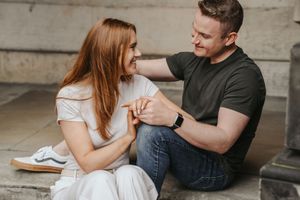A couple sits close together on a concrete surface sharing an intimate moment in casual clothing.