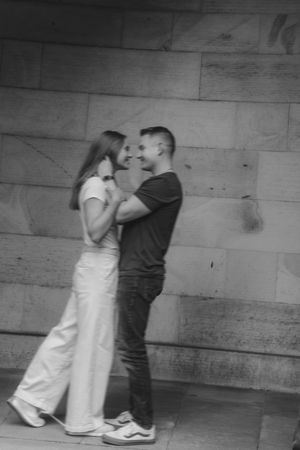 A couple shares a romantic moment against a rustic wooden wall in black and white photography.