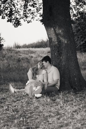 Romantic couple sitting together under a large tree in black and white photography.