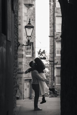 A romantic black and white silhouette of a couple embracing on a historic cobblestone street with a vintage lamp post.