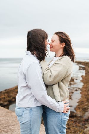 A romantic seaside embrace between two people wearing jeans and casual tops on a rocky coastal path.