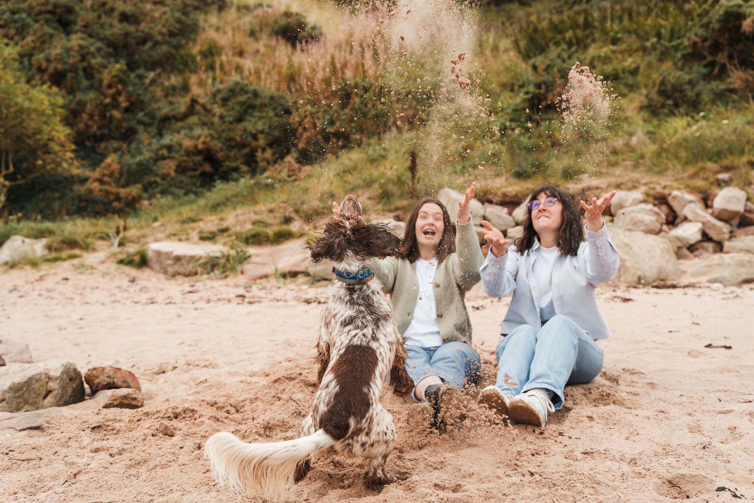 Friends sitting together on a rocky beach shore during a cloudy day while wearing casual outfits.