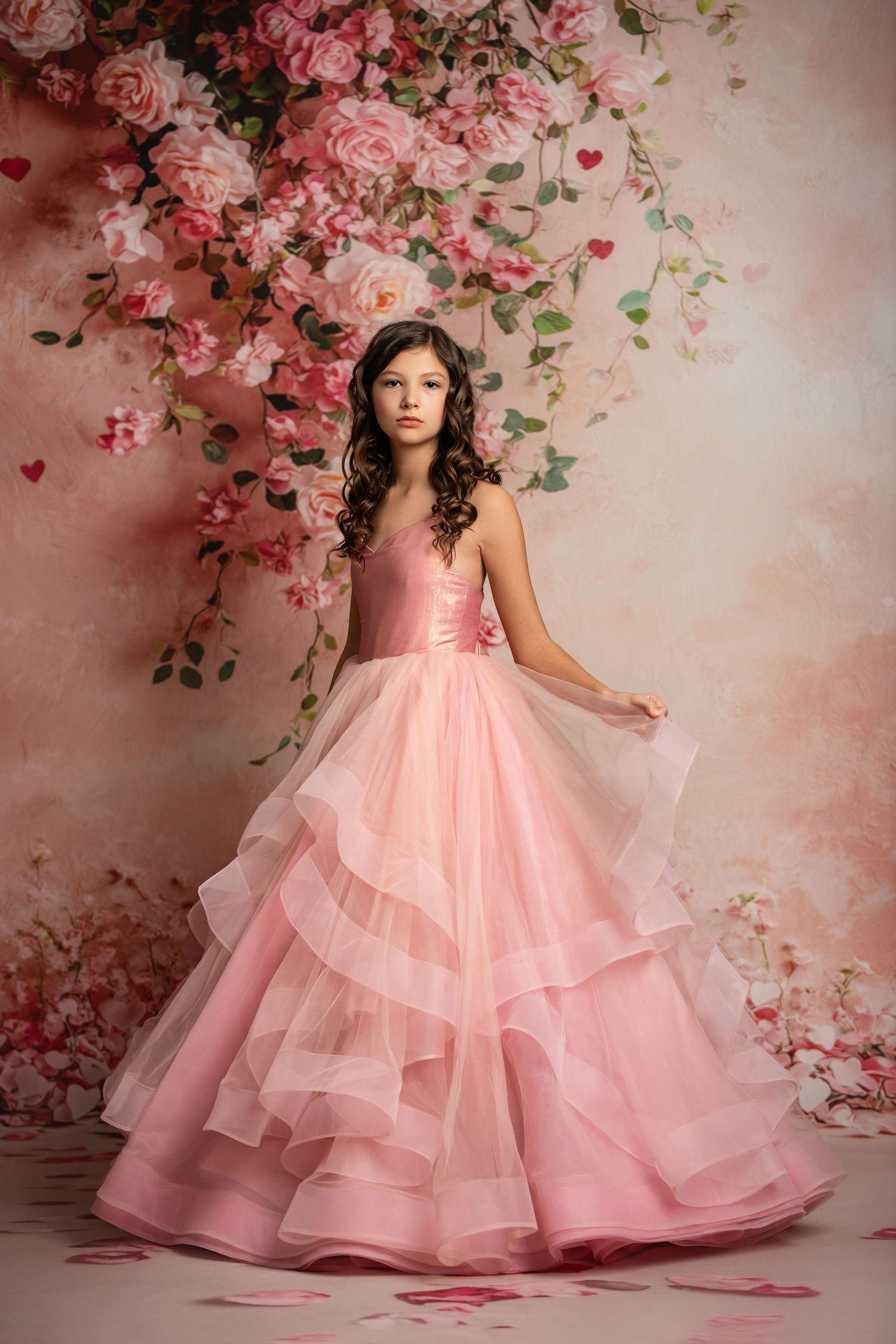 Elegant pink ballgown with layered tulle skirt against floral backdrop.