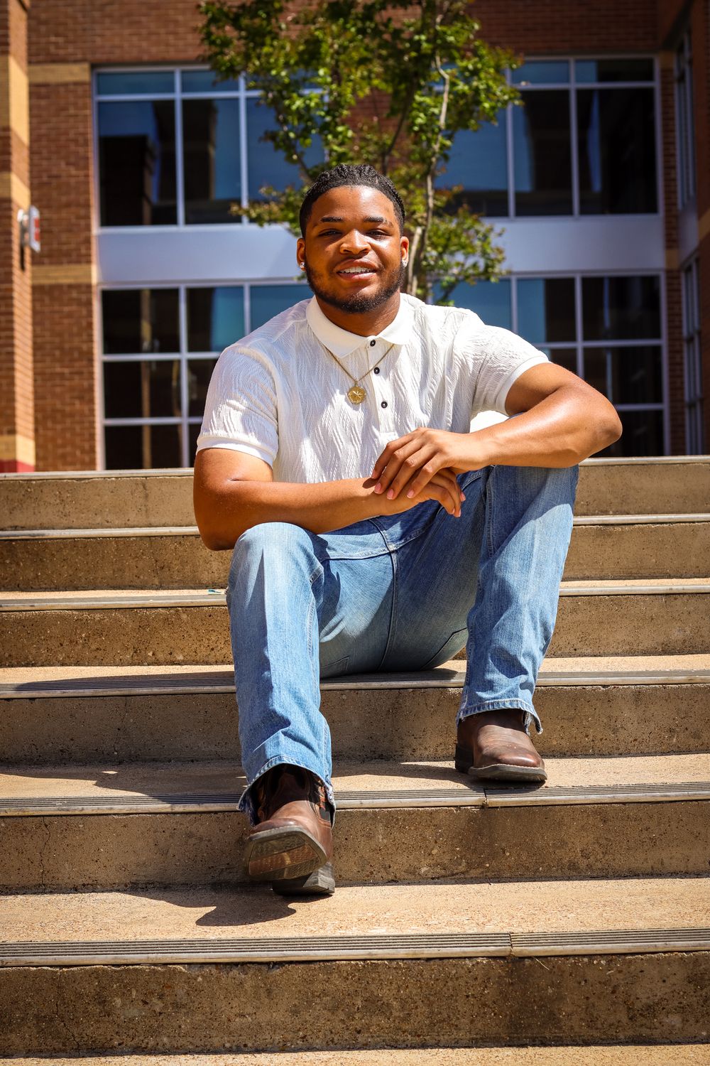 Young Black man smiling on outdoor steps in white shirt and jeans.