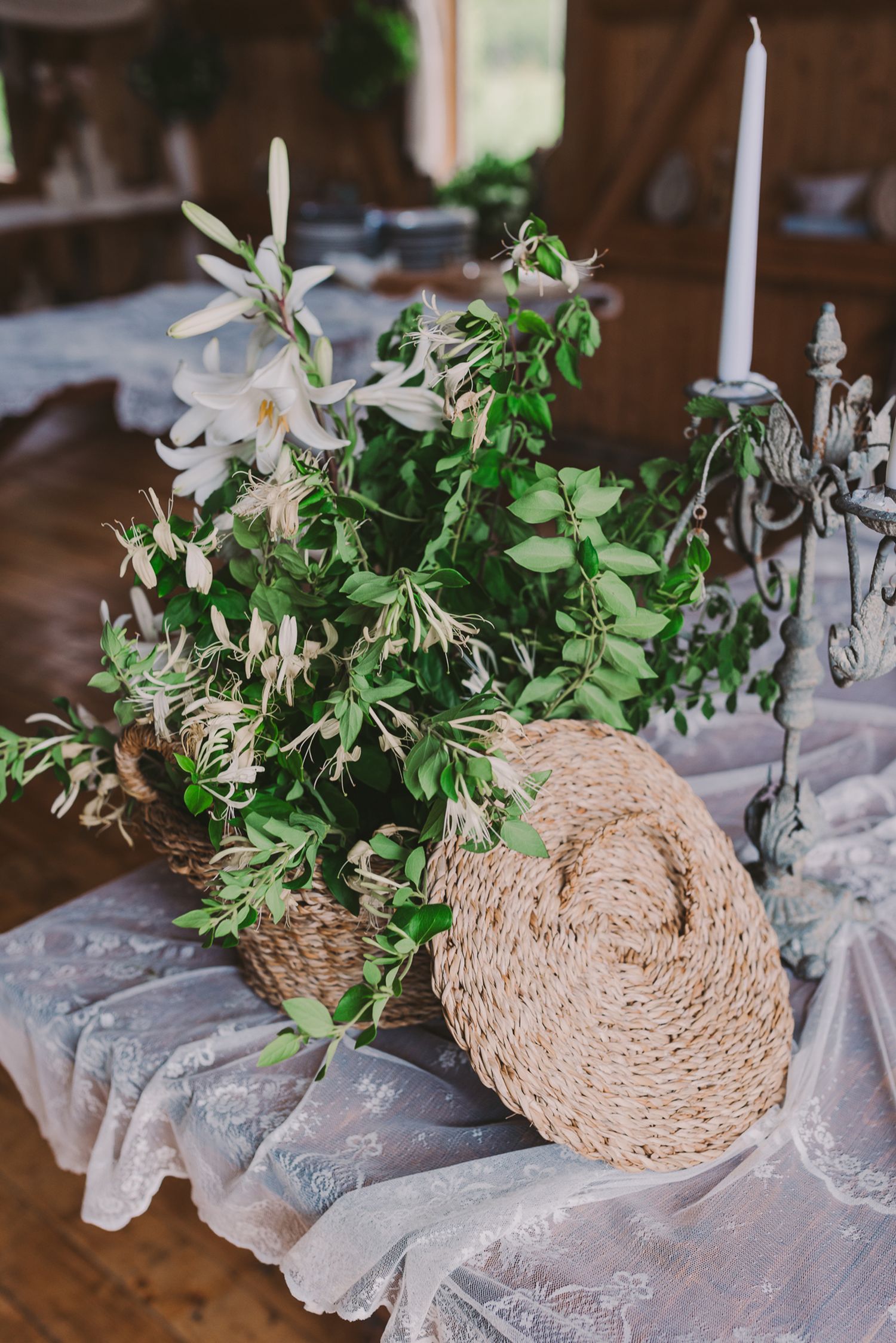 Wedding table centerpiece with woven base, greenery, and white candles.