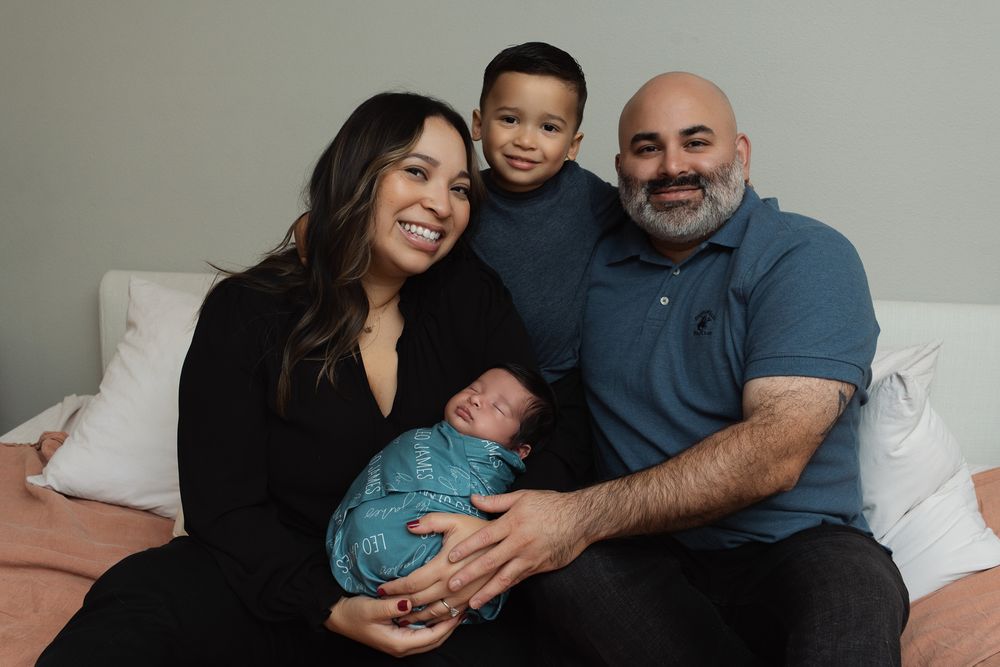 A family sits together on a bed while holding a newborn baby in various poses and tender moments.