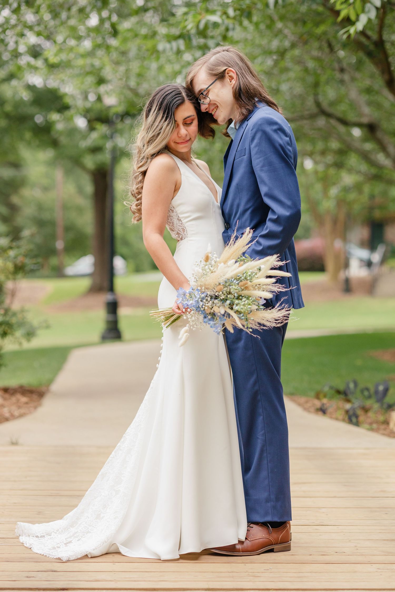 A couple shares an intimate moment on a pathway while the bride holds a dried flower bouquet.