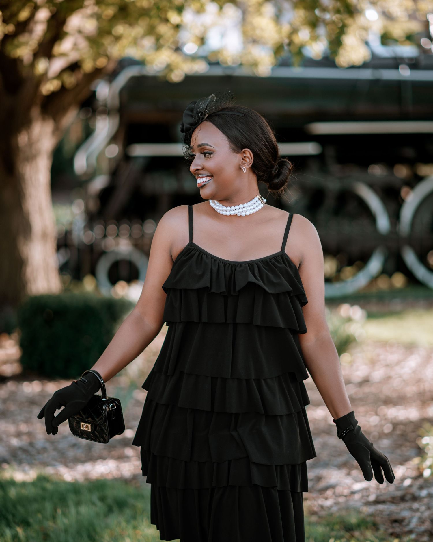 Fashion photoshoot in a park setting featuring a black ruffled dress and elegant accessories.