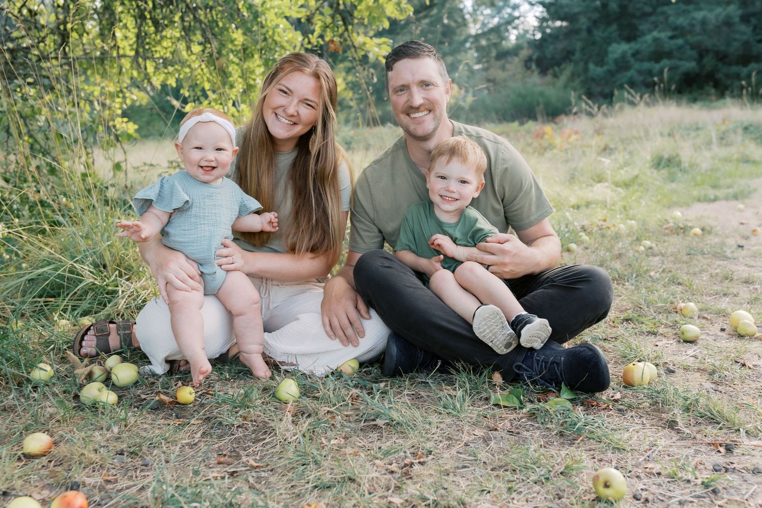 Happy family of four sitting together under an apple tree in a meadow.