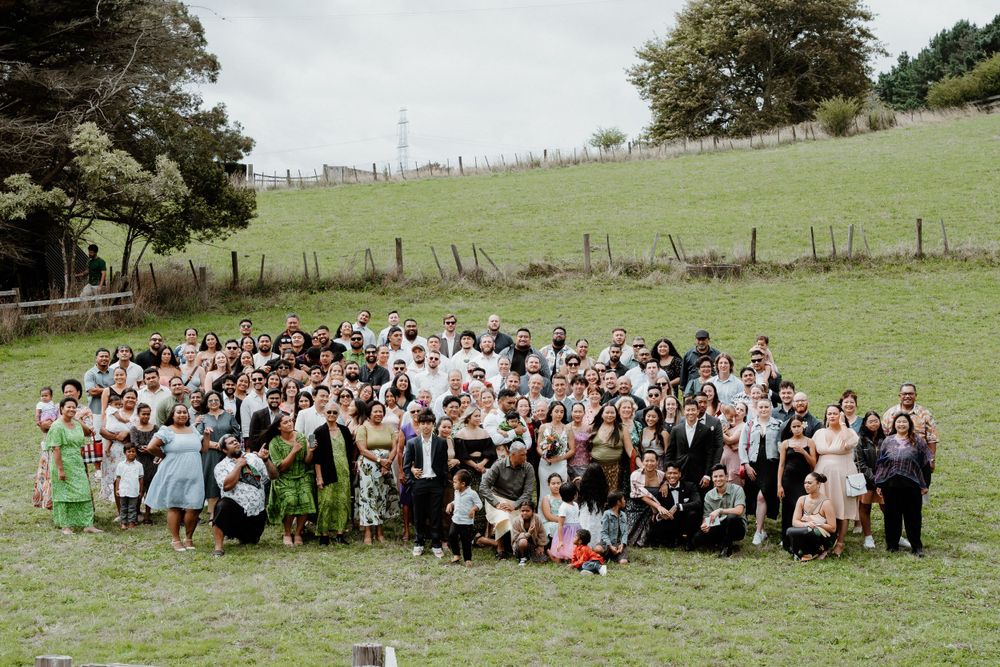Large group wedding photo of guests and wedding party on a grassy hillside.