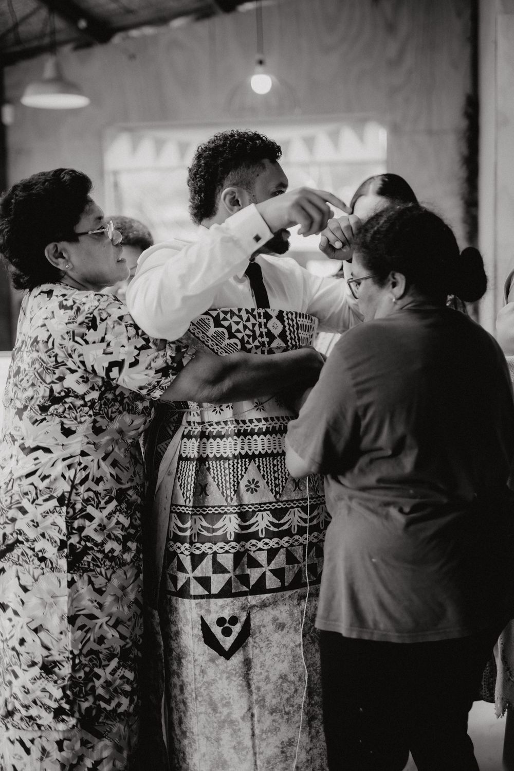 Black and white photo of group helping dress someone in traditional cultural attire.