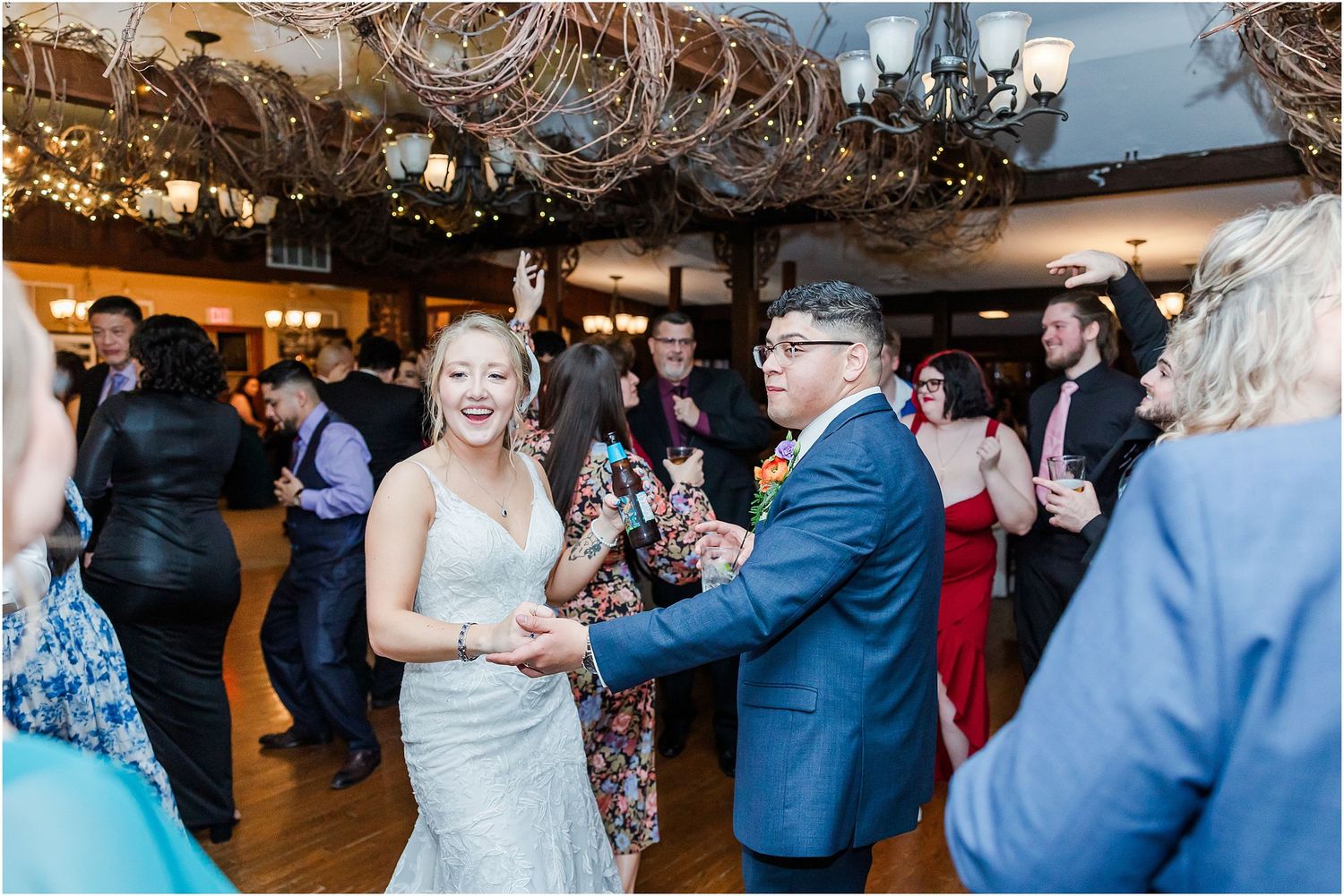 Guests mingle and celebrate during a wedding reception under decorative lights and chandeliers.