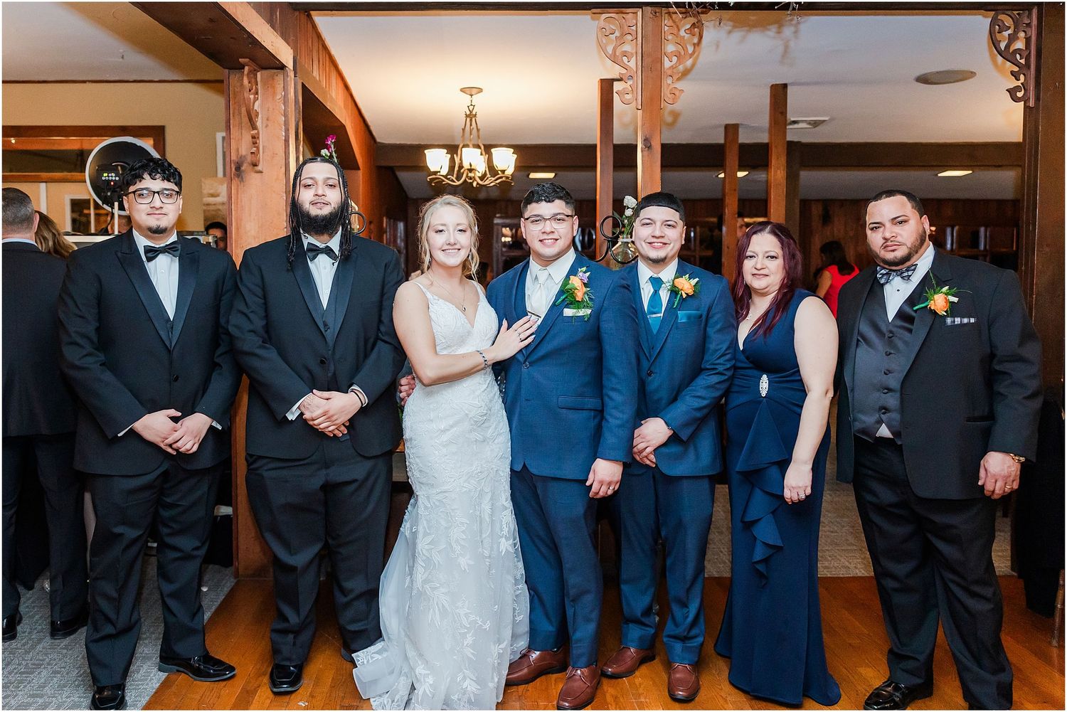 Wedding party members pose together in formal attire inside an elegant wood-paneled venue.
