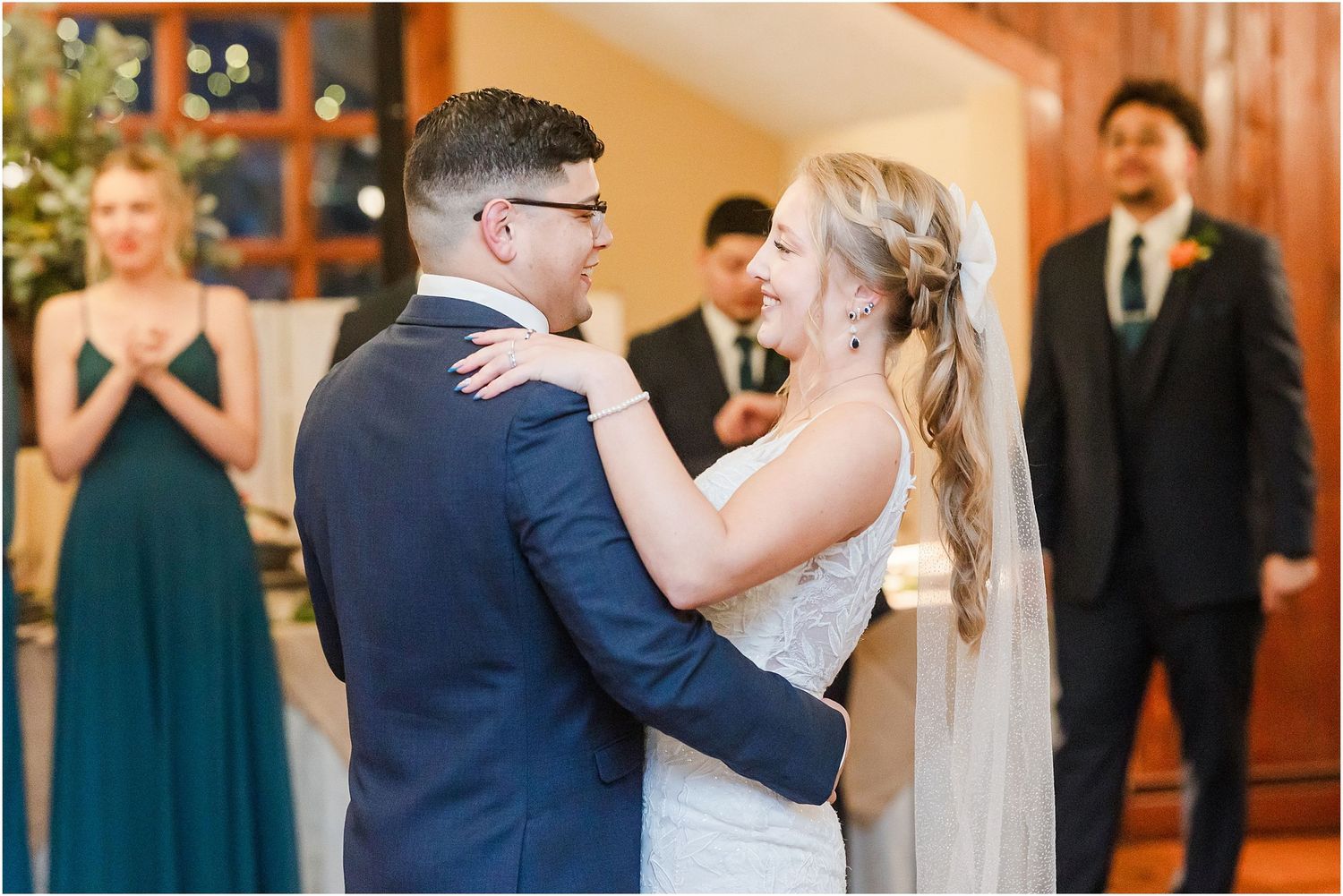 Romantic first dance moment between newlyweds with wedding party watching in background.