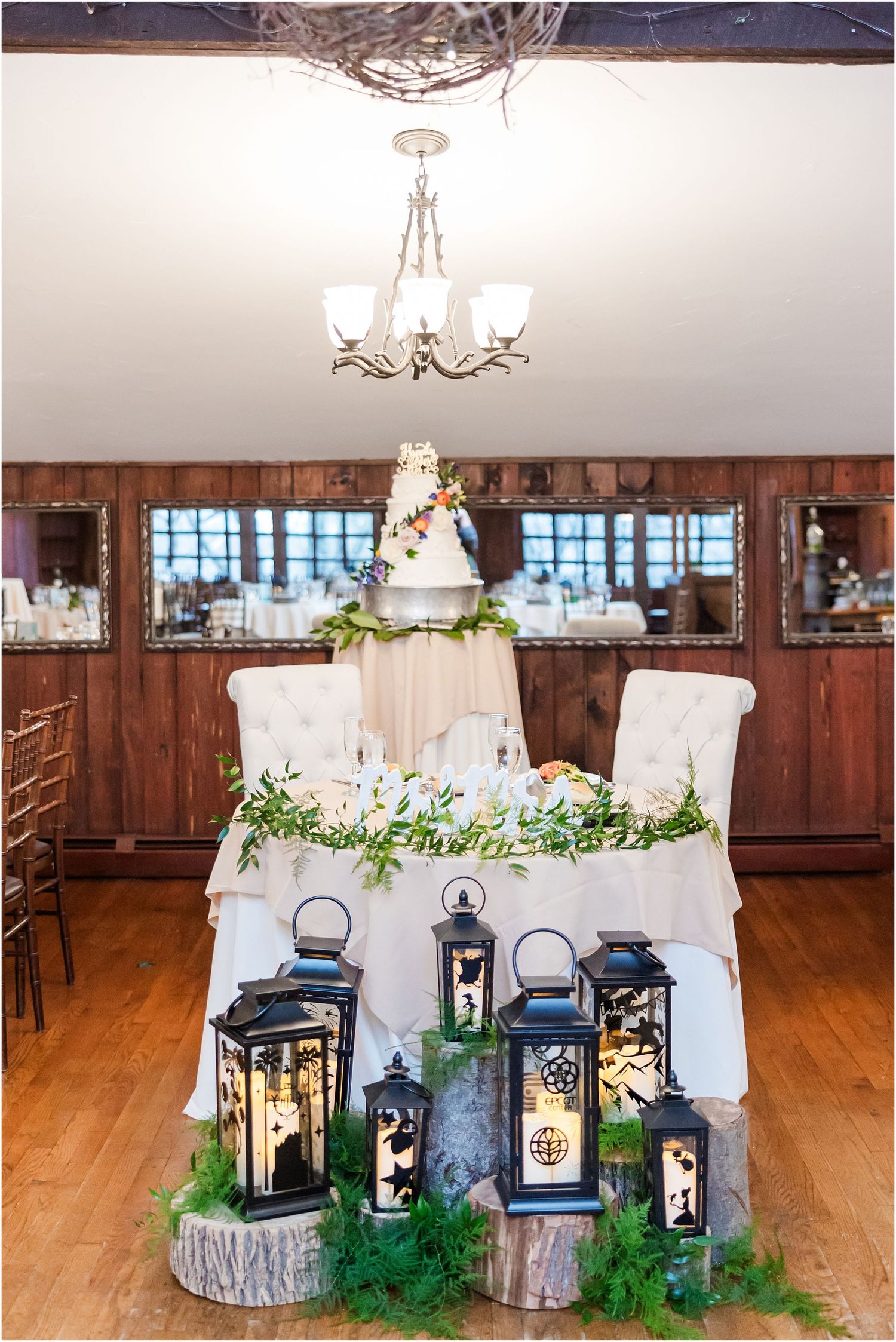 Wedding cake display with decorative lanterns and greenery on rustic wood slices.