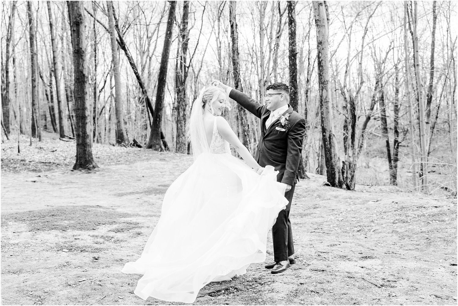 Black and white photo of newlyweds dancing together in a wooded outdoor setting.