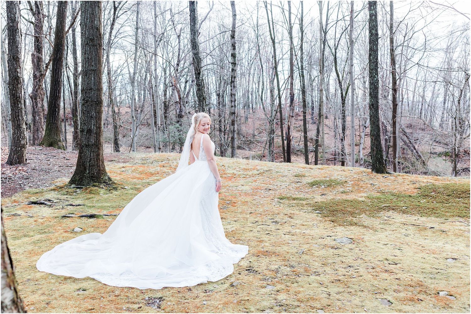Long wedding dress train flowing across autumn forest ground in ethereal bridal portrait.