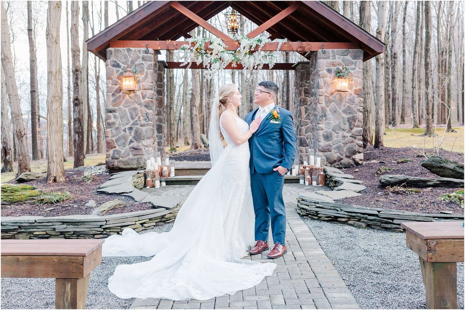 Couple sharing a romantic moment under a stone pavilion with wooden beams in a forest setting.