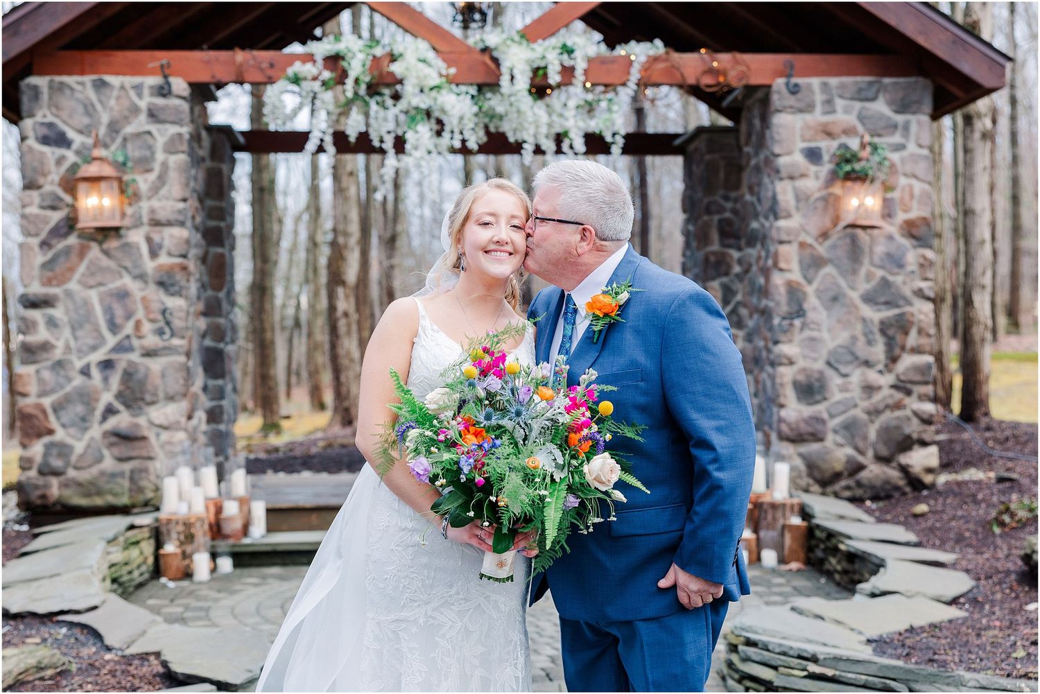 Intimate moment between couple in front of stone chapel with colorful bridal bouquet.