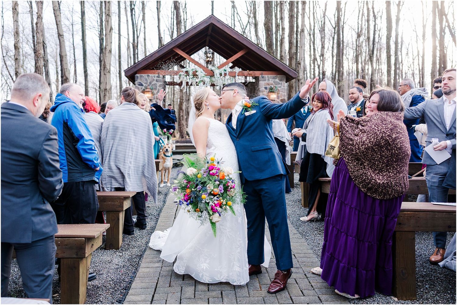 Wedding couple shares first dance under wooden pavilion while guests watch and celebrate.