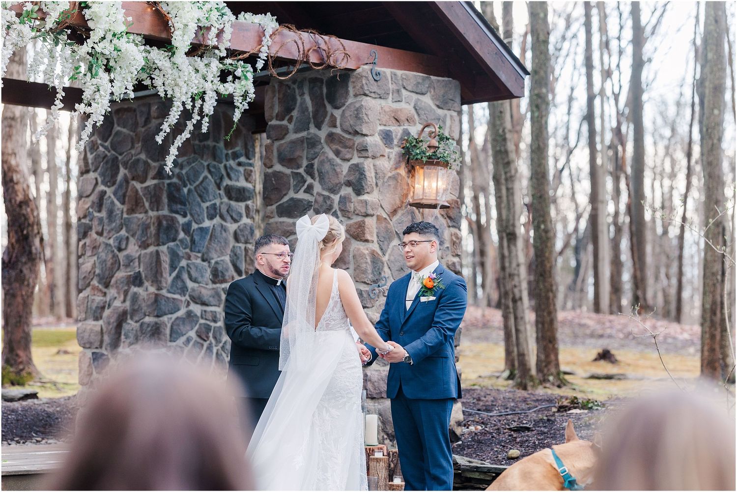 Couple exchanges vows at rustic stone pavilion decorated with hanging greenery.