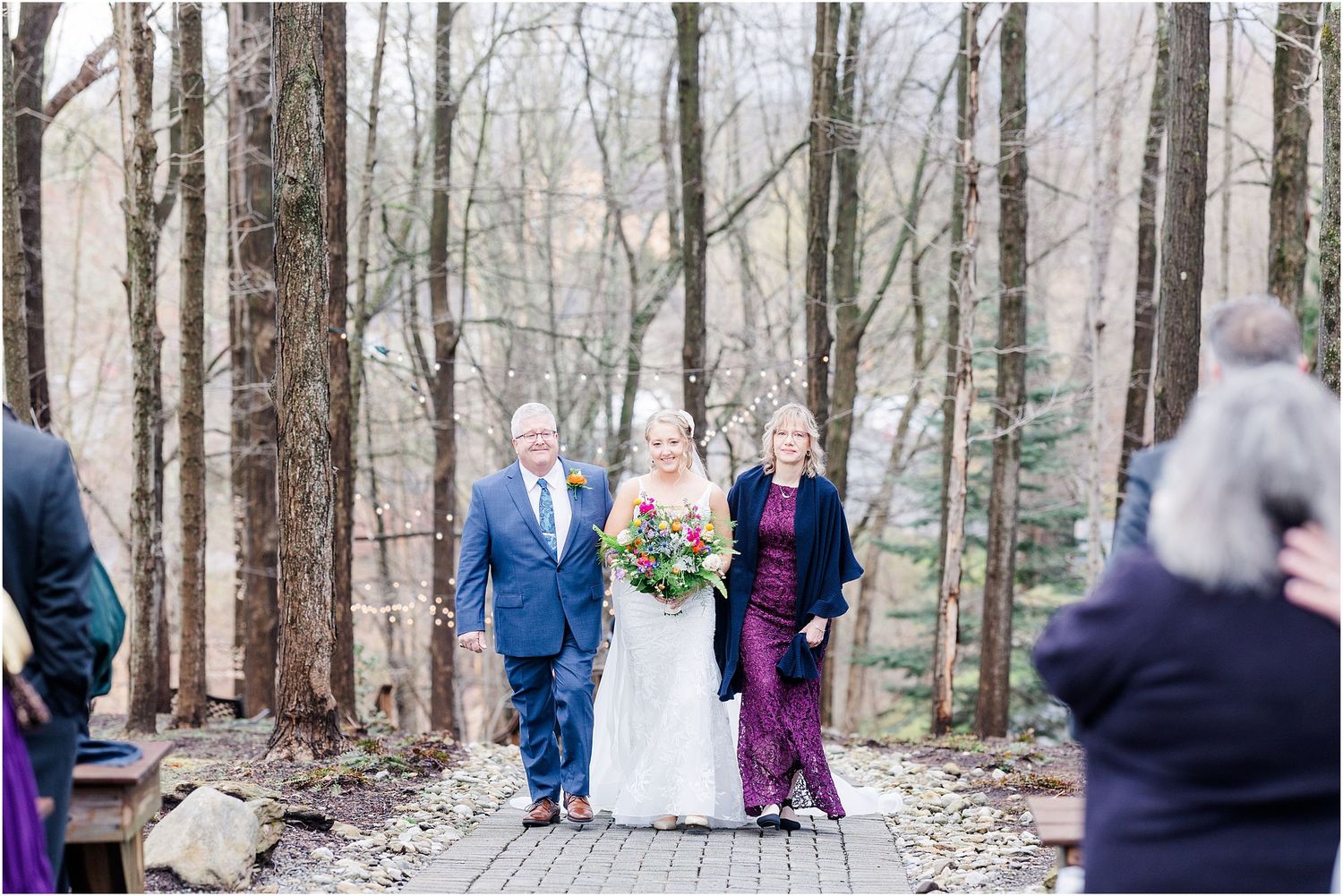 Wedding party walking down wooden pathway surrounded by bare winter trees.
