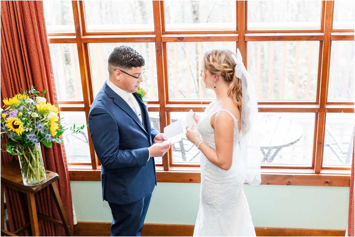 Couple exchanges rings during intimate wedding ceremony by large wooden-framed windows.