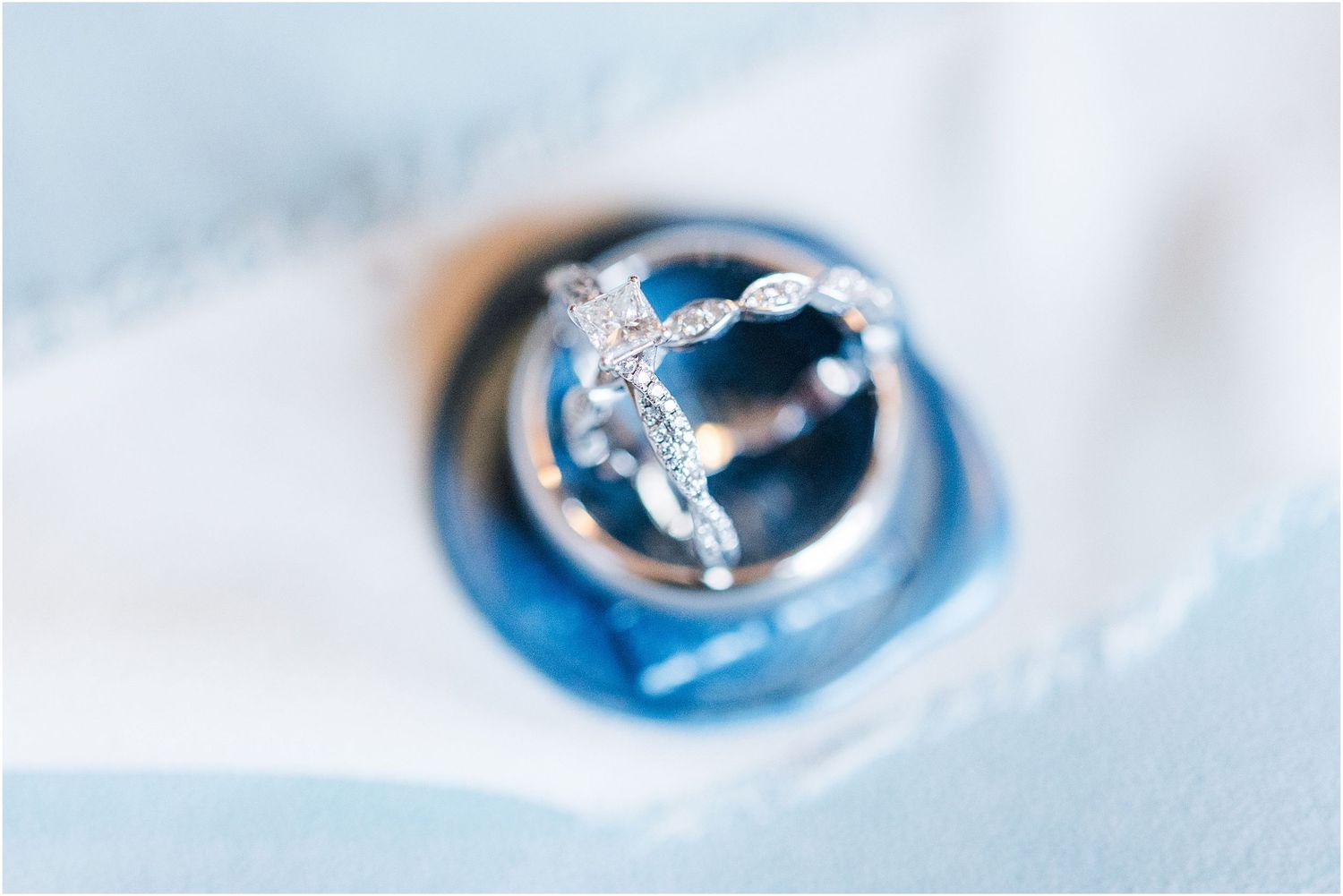 A detailed macro shot of a silver wedding ring with a decorative pattern against a blurred blue background.