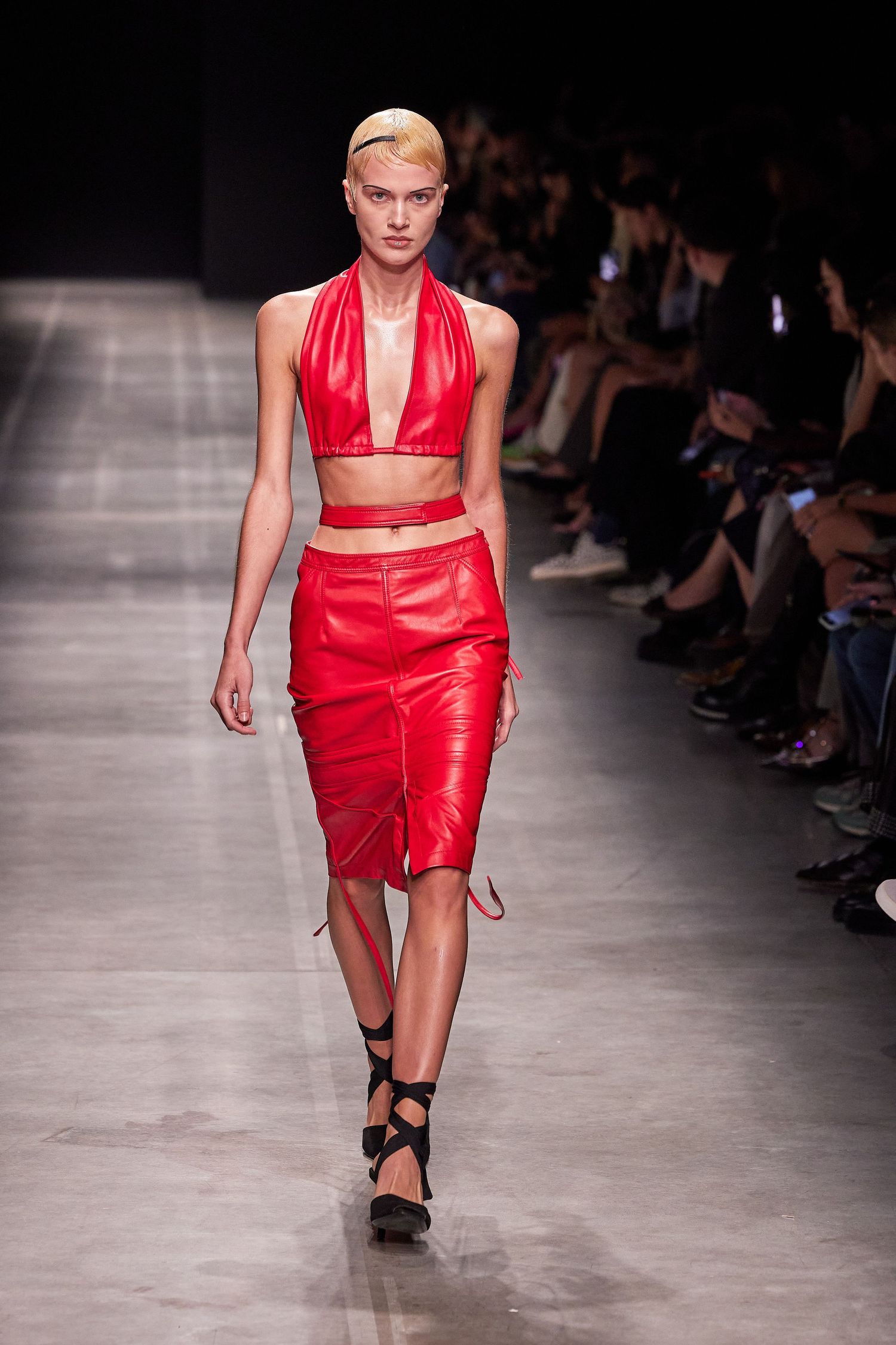 Fashion runway show featuring a red leather two-piece ensemble on a concrete catwalk.