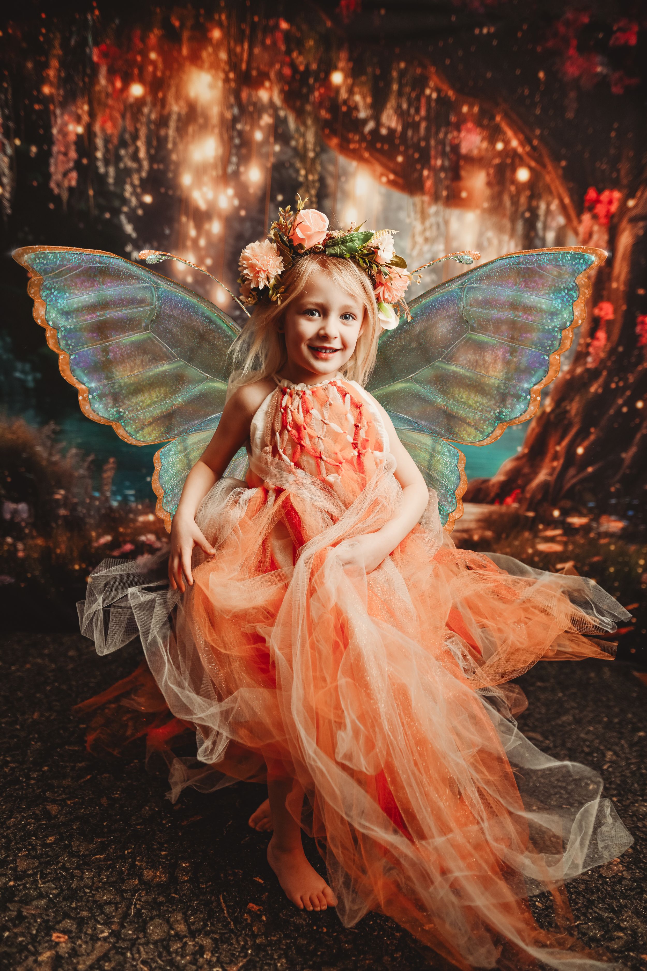 Magical fairy photoshoot in enchanted forest with teal wings and peach tulle dress against glowing bokeh lights.