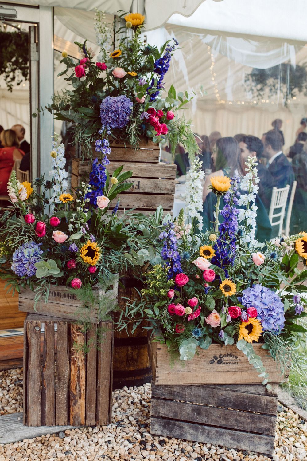 Rustic wooden crates display colorful wildflower arrangements with sunflowers and purple delphinium.