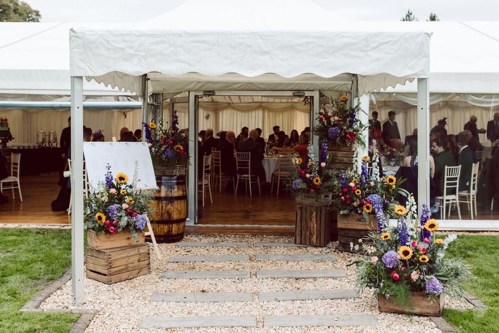 White wedding tent set up on gravel with rustic floral decorations and wooden crates.