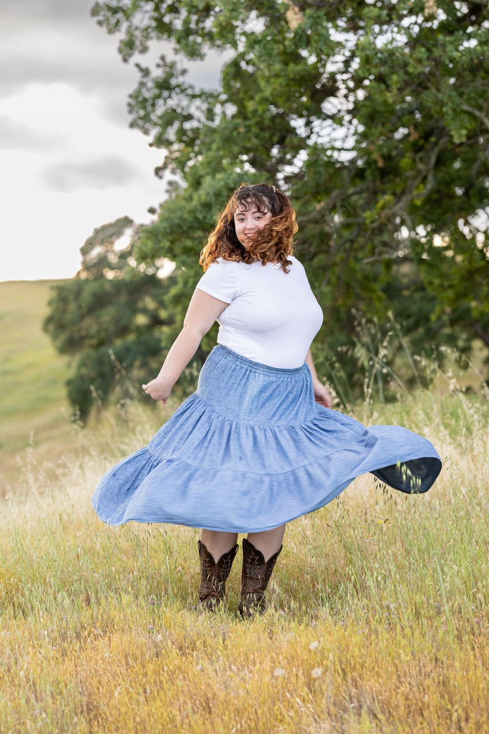 A joyful twirl in a flowing blue skirt and cowboy boots captures a carefree moment in a sunlit meadow.