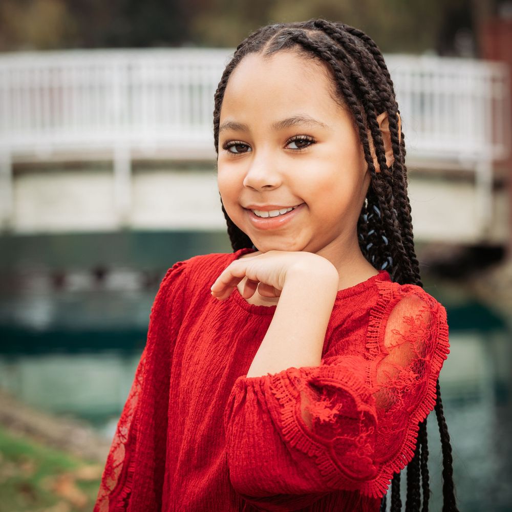 Person in a vibrant red sweater smiling warmly while posing outdoors against a natural background.