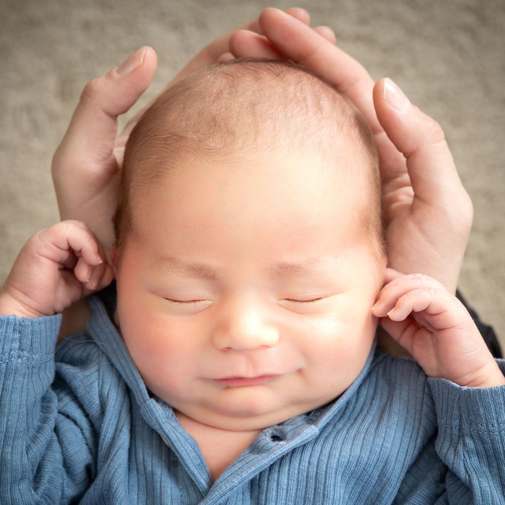 Peaceful sleeping baby in blue sweater with hands gently cradling their head.