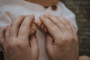 Two hands hold each other in a tender embrace against a dark green background.